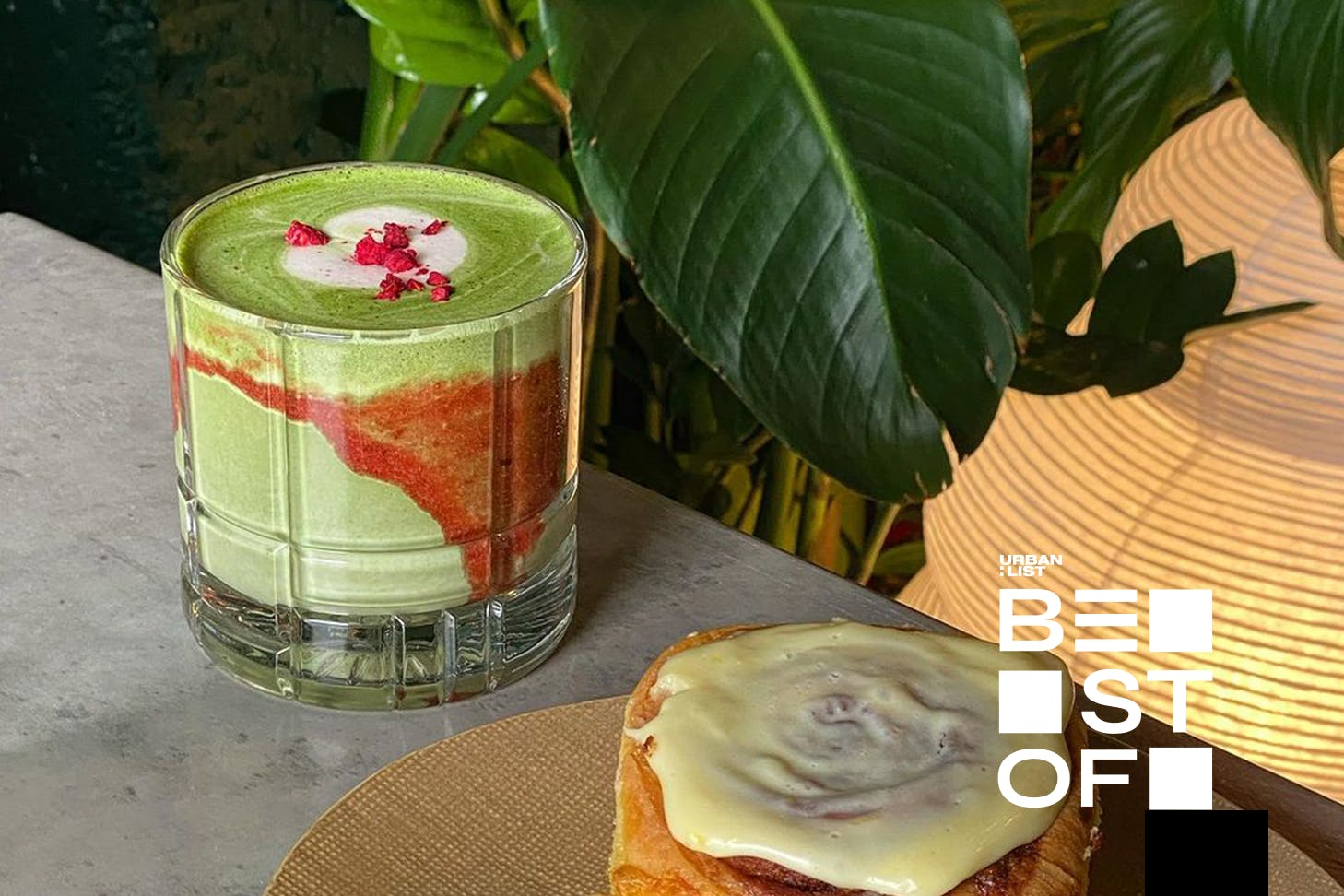 A glass of strawberry matcha beside a sticky bun.